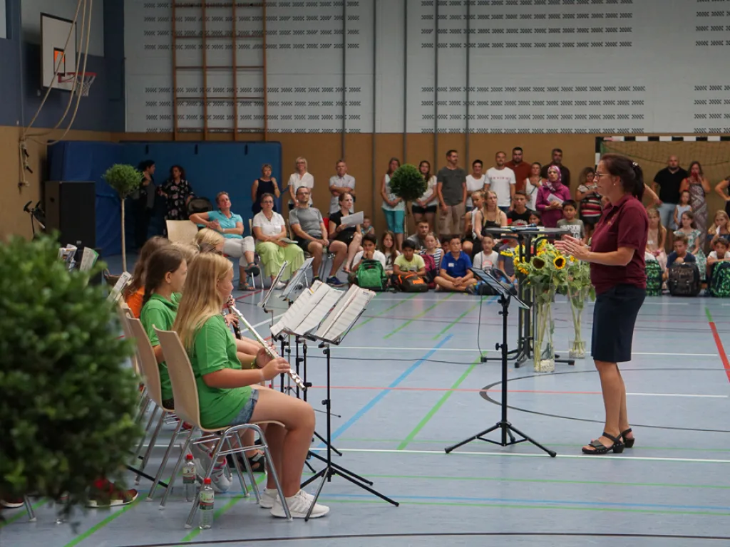 Person dirigiert das Orchester vor Blumen.